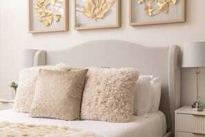 A bedroom with a bed, fluffy pillows, a nightstand, a lamp, and wall art.