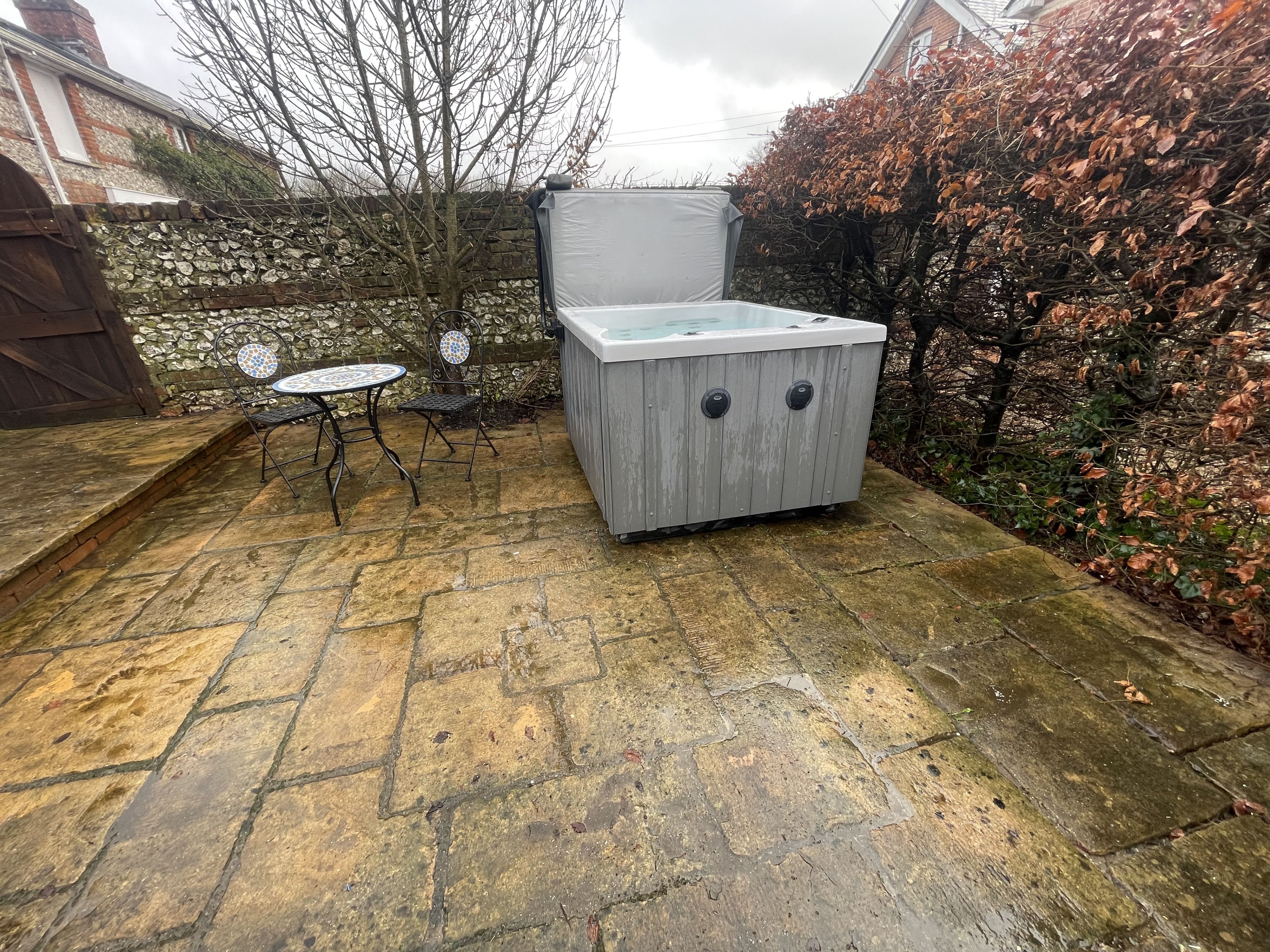 Une terrasse en pierre avec un jacuzzi, une petite table ronde et deux chaises.