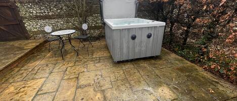 Une terrasse en pierre avec un jacuzzi, une petite table ronde et deux chaises.