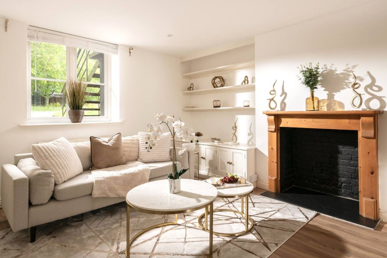 A living room with a sofa, two side tables, a fireplace, and a window with a plant.