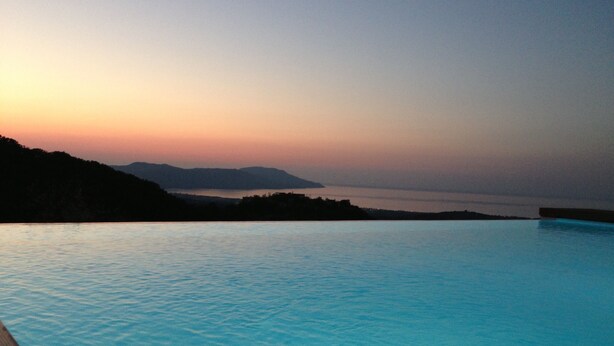 Une piscine à débordement paisible, offrant une vue dégagée sur l’eau et les montagnes lointaines au coucher du soleil.