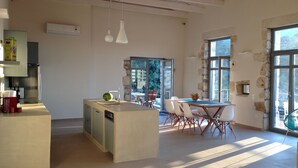 Une cuisine moderne dotée d’un îlot central, d’un coin repas avec une table et des chaises, et de grandes fenêtres laissant entrer la lumière naturelle.