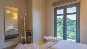 Une chambre d’hôtel avec un lit, une grande fenêtre donnant sur un espace verdoyant, un miroir et un porte-serviettes.