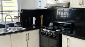A kitchen with white cabinets, a black countertop, a stainless steel sink, and a gas stove.
