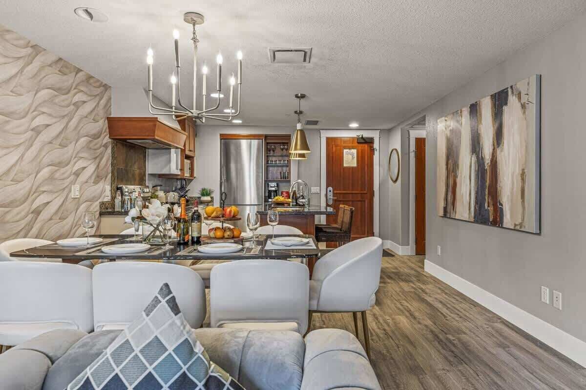 A modern dining area with a chandelier, a dining table set for four, and a sofa with cushions.