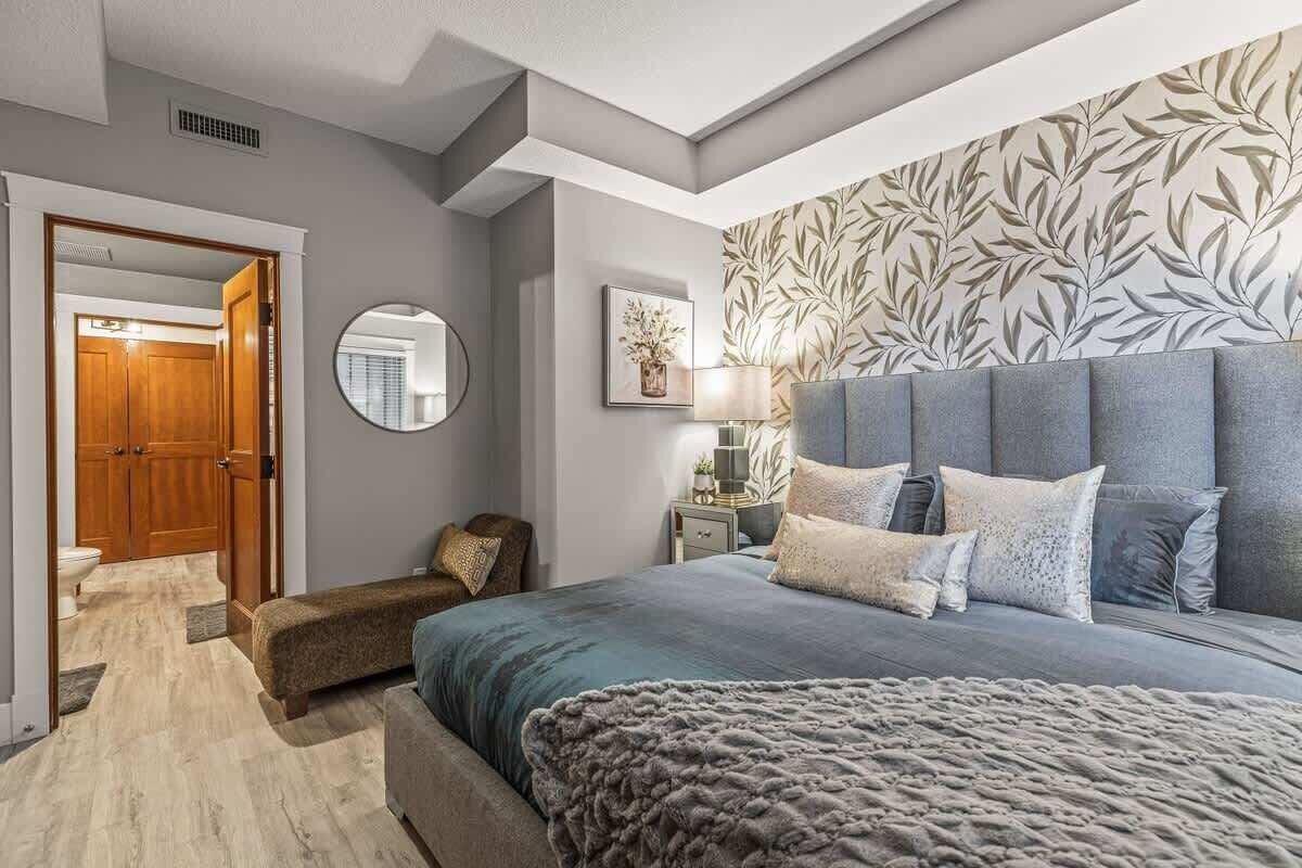 A bedroom with a large bed, a bedside table with a lamp, a mirror, and a wall with a leaf pattern.