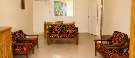 A room with a sofa set, a dining table, and chairs, a window with a view of trees, and an air conditioning unit.