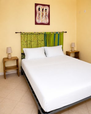 Un dormitorio con cama, dos mesitas de noche, un cuadro colgado en la pared y cortinas.