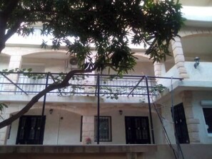 A building with a balcony, a tree in front, and a clear view of the street.