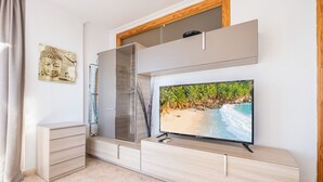 A modern living room with a flat-screen TV, a wooden cabinet, and a glass door closet.