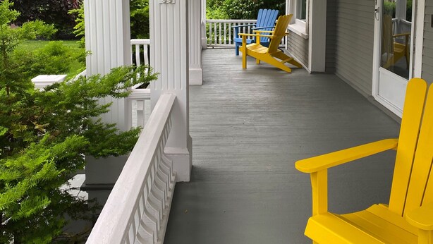 A porch with a hanging flower basket, a yellow Adirondack chair, and a blue Adirondack chair. - The Boardwalk Inn  (Summerside)