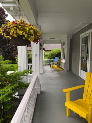 A porch with a hanging flower basket, a yellow Adirondack chair, and a blue Adirondack chair. - The Boardwalk Inn  (Summerside)