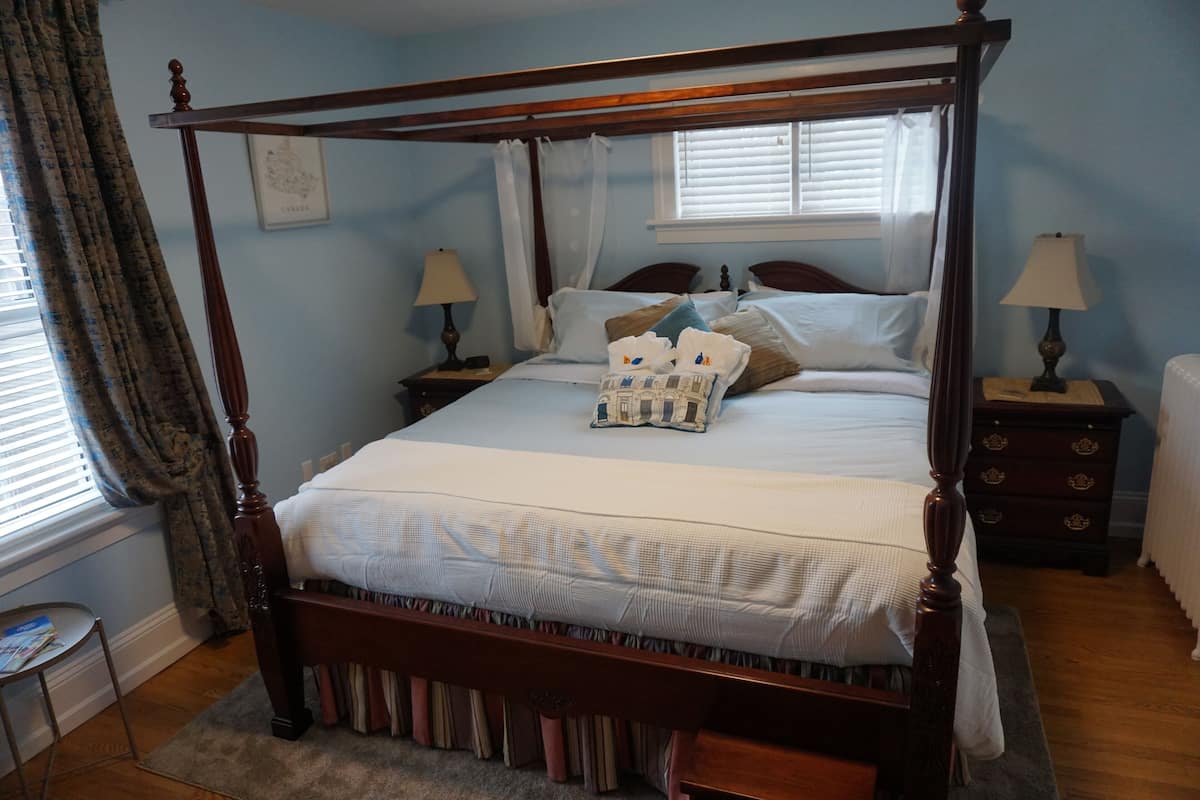 Una cama con dosel de madera, ropa de cama blanca y una mesita de noche con lámpara.