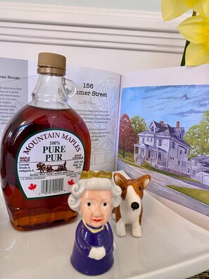 A bottle of Mountain Maple Pure Syrup, a ceramic figurine, and a book with a house illustration.