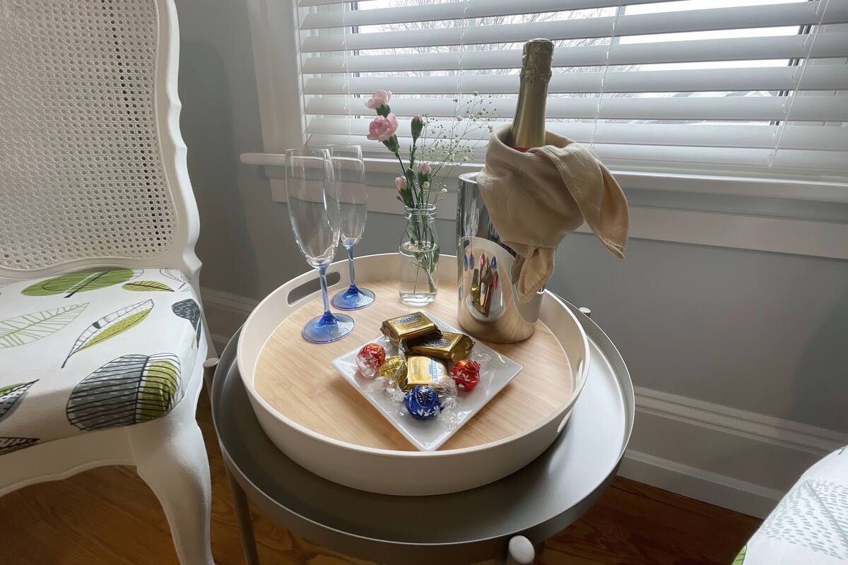 Una mesa con una botella de champán, dos copas, un florero con flores y un plato con bombones.