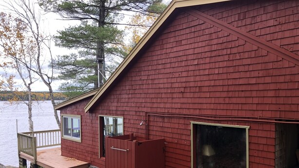 A red wooden cabin with a dock, large windows, and a view of a lake.