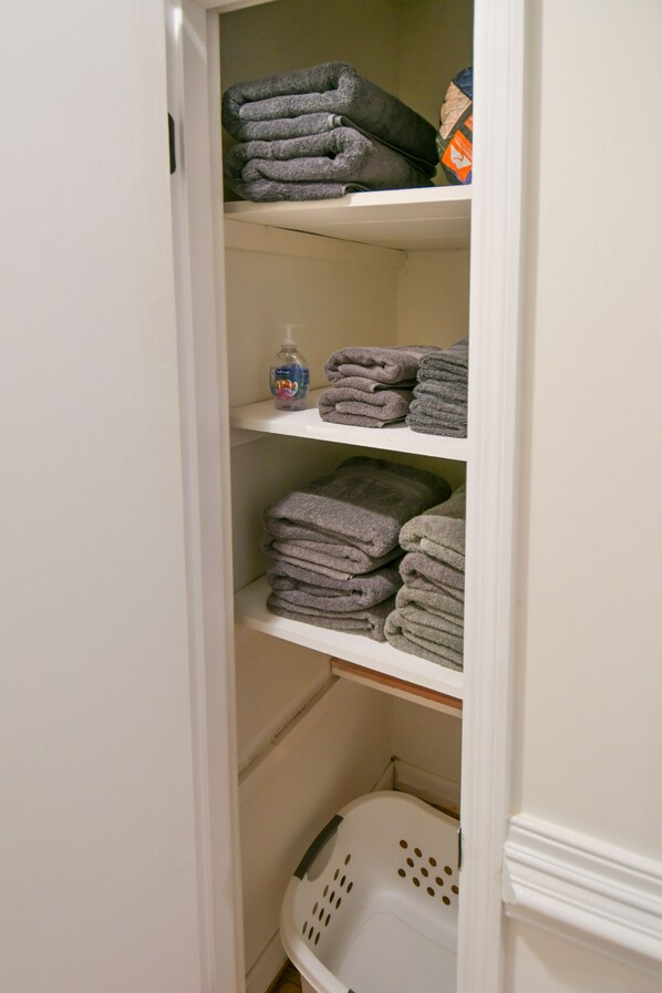 A white closet with shelves holding folded towels and a laundry basket.