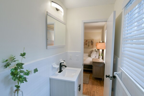 A bathroom with a white sink, a mirror, and a plant.