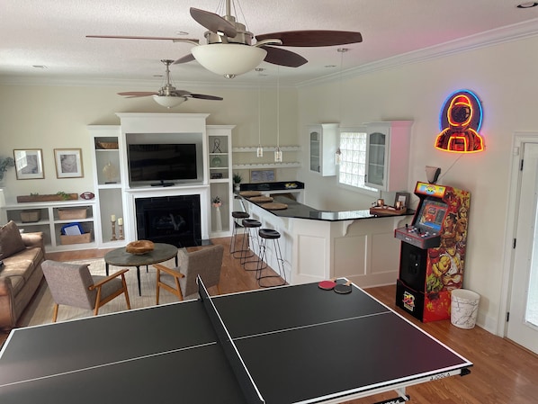 A living room with a ping pong table, a TV, and a neon sign. - Luxurious 3 BR/2 BA w/ Patio Deck, Wet Bar, Ping-Pong, Arcade, & King Bed (Columbia)