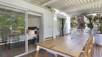 Une vaste terrasse dotée d’une table et de chaises en bois, une porte-fenêtre coulissante donnant sur un balcon et une grande plante en pot.