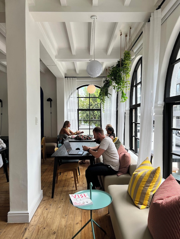 A spacious room with a large window, a round table with a laptop, and a sofa with striped pillows. - Neighbourgood Hill (Cape Town)