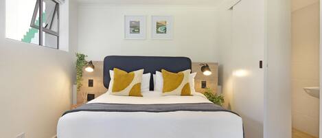 A modern bedroom with a large bed, two framed pictures on the wall, and a window with a view of stairs.