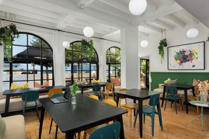 A modern cafe with tables and chairs, large windows, and hanging plants. - Neighbourgood Hill (Cape Town)