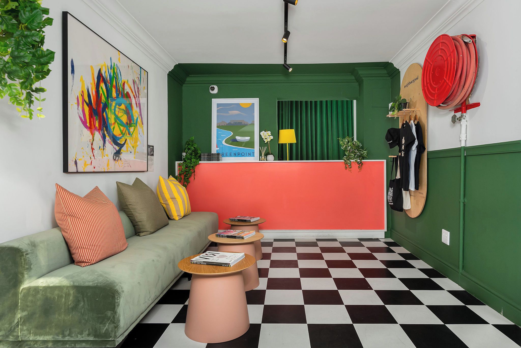 Une pièce avec un canapé vert, un sol à carreaux, un comptoir d’accueil rouge et un tableau au mur.