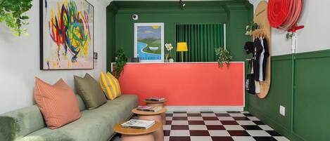 Une pièce avec un canapé vert, un sol à carreaux, un comptoir d’accueil rouge et un tableau au mur.