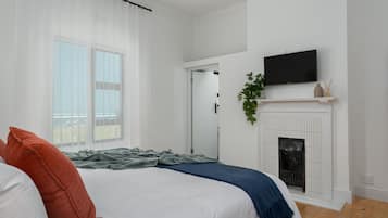 Un dormitorio con cama, chimenea, televisión y ventana con cortinas.