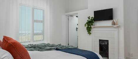 A bedroom with a bed, a fireplace, a television, and a window with curtains.