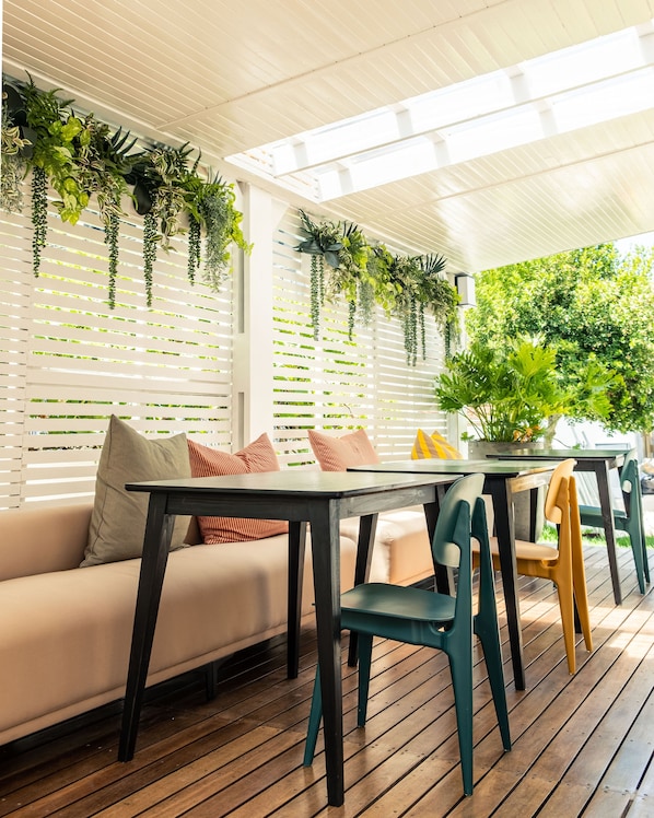 Un patio al aire libre con piso de madera, un sofá con cojines, una mesa y sillas.