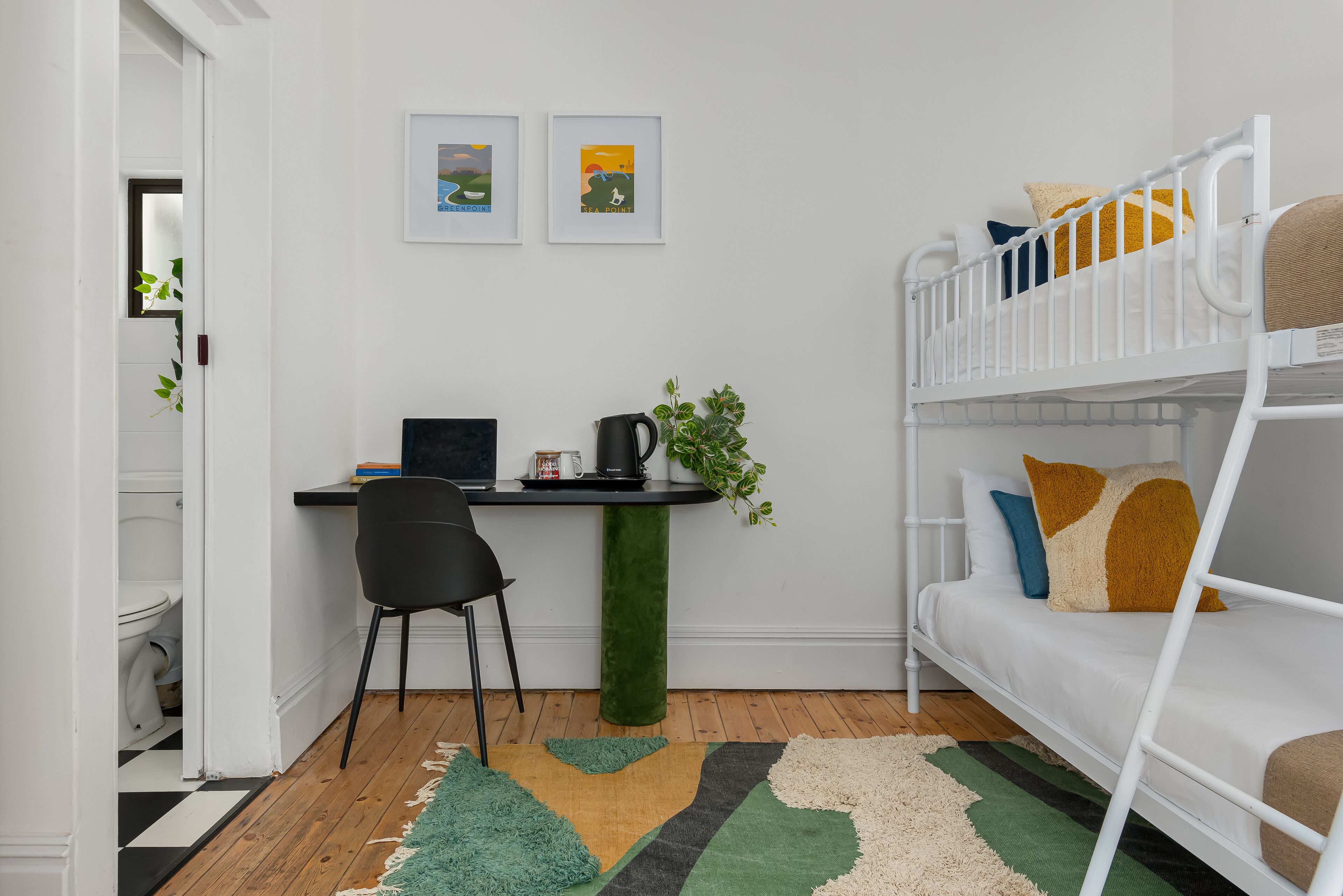 Une chambre avec un lit superposé, un bureau avec un ordinateur portable, une chaise, une machine à café et une plante.