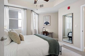 Un dormitorio con una cama grande, un escritorio, una silla, un espejo y una ventana con cortinas.