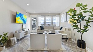A modern living room with a sofa, two white armchairs, a coffee table, and a large window with a view. - Sparks Marina 2BR · Waterfront Views & Jacuzzi (Sparks)