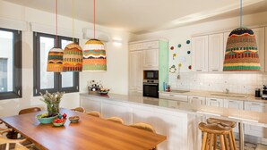 A modern kitchen with white cabinets, a wooden dining table, and colorful hanging lights. - TIMORI, modern, panorama views, pool & kiddie-pool, 4 bedrooms plus guest house. (PLAKA)