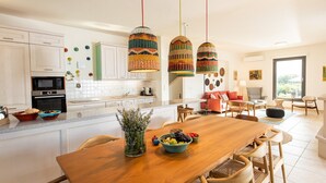 A modern kitchen with white cabinets, a wooden dining table, and colorful woven pendant lights. - TIMORI, modern, panorama views, pool & kiddie-pool, 4 bedrooms plus guest house. (PLAKA)