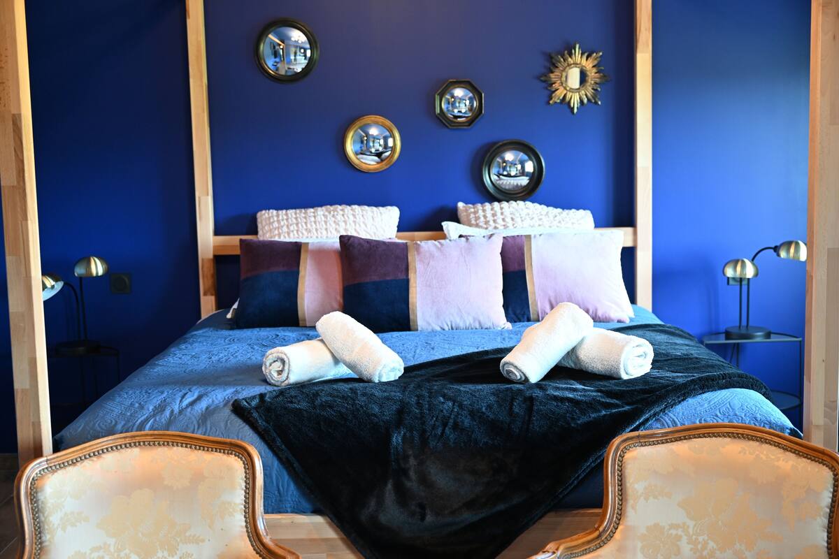 Ein Schlafzimmer mit einem großen Bett, vielen Kissen, einer dunkelblauen Wand und einem Spiegel.