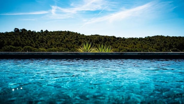 Une piscine d’eau cristalline offrant une vue sur une colline boisée.