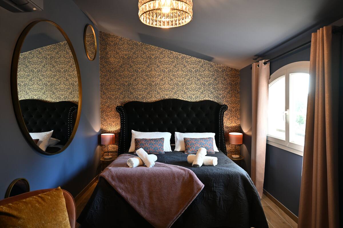 Ein Schlafzimmer mit einem großen Bett, zwei Nachttischen, einem Spiegel und einer Kandelaber.
