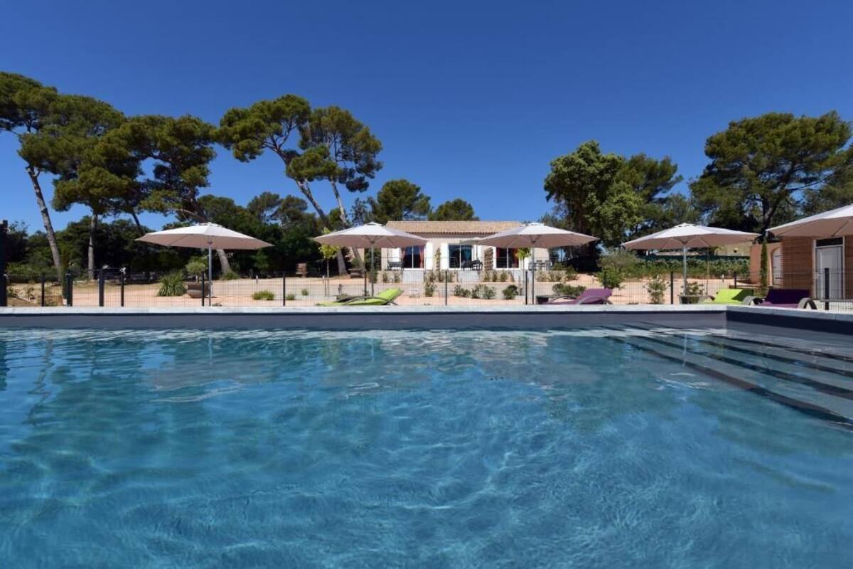 Ein Pool mit Liegestühlen und Sonnenschirmen, umgeben von Bäumen und einem Gebäude mit Ziegeldach.
