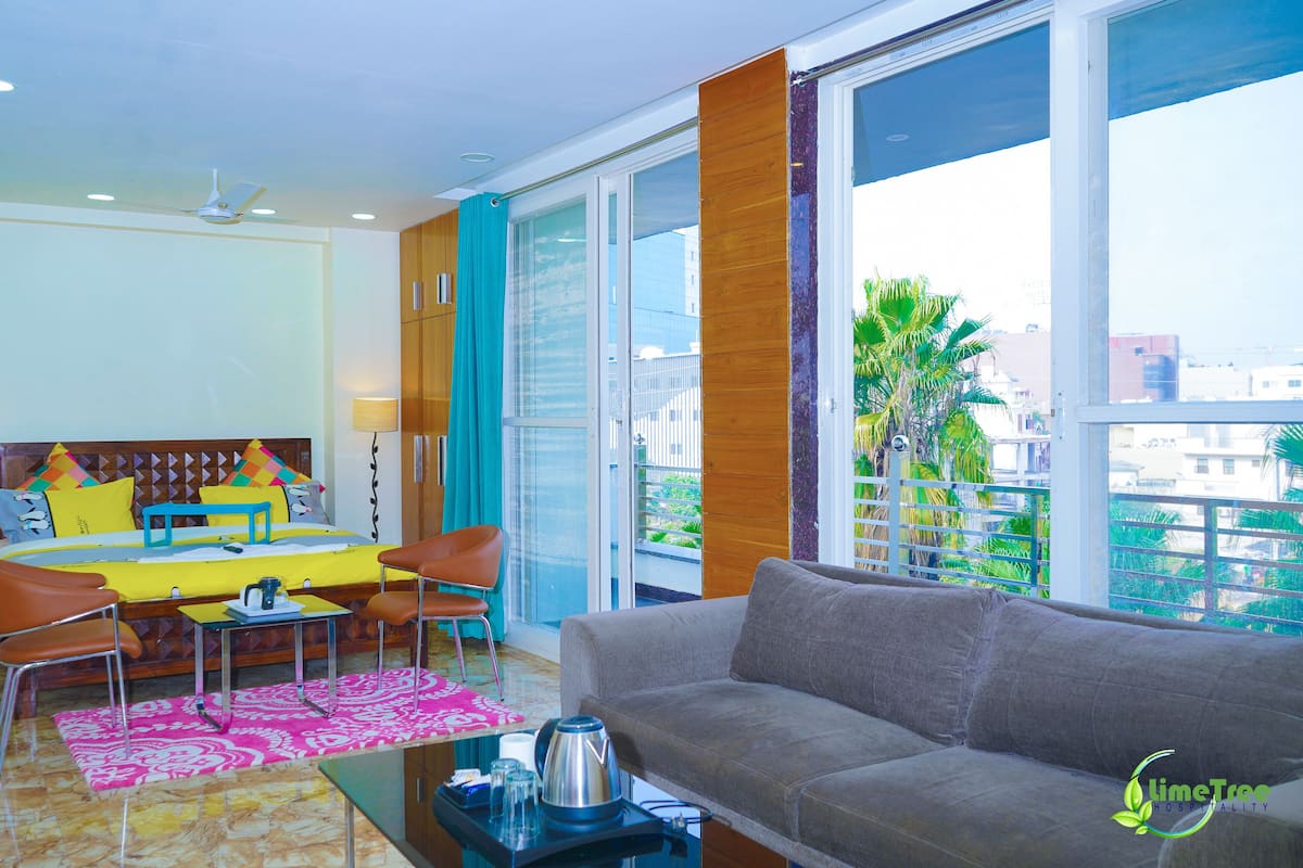 Habitación de hotel moderna con sofá, mesa de comedor, sillas y balcón con vista a la ciudad.