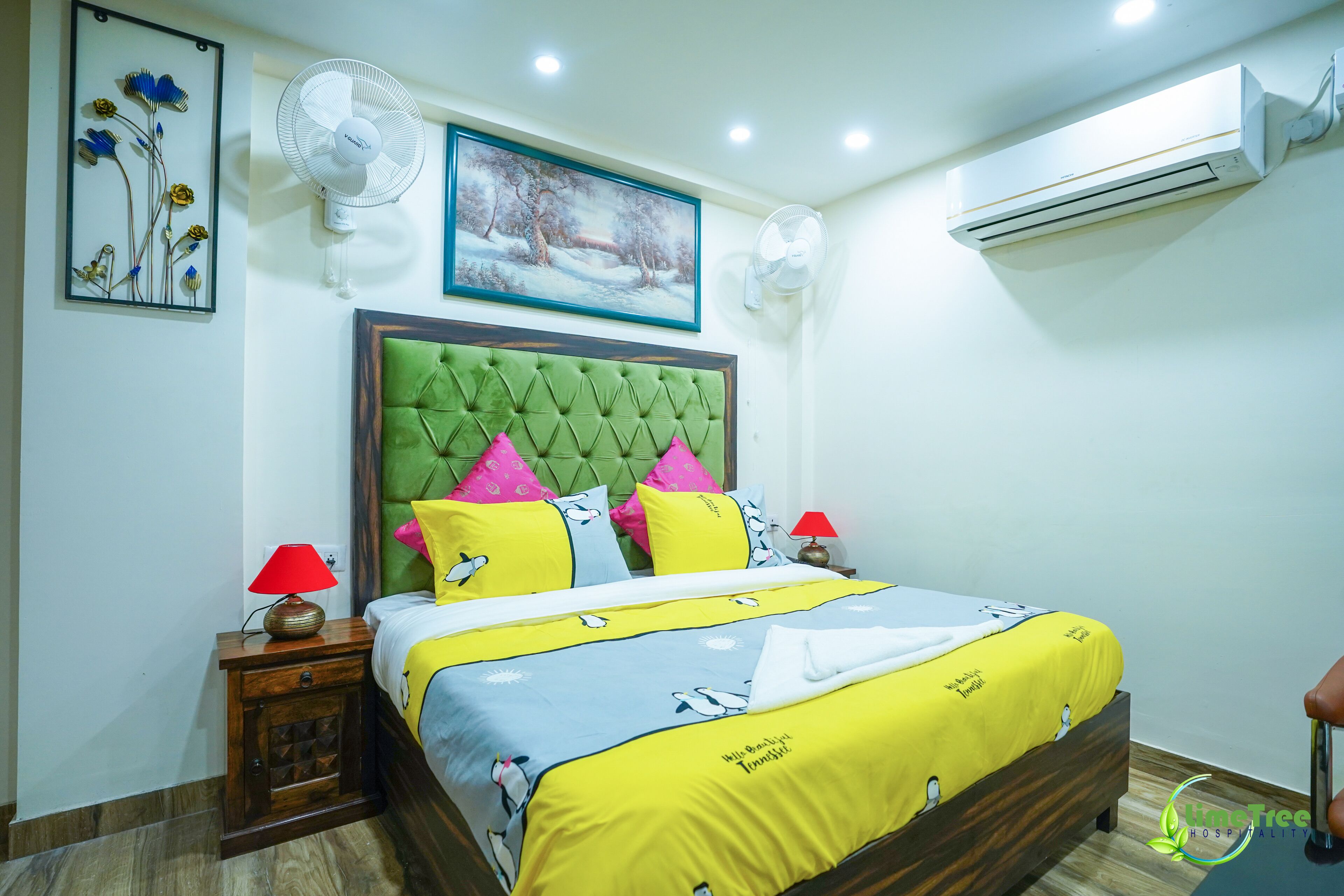 A neatly arranged bedroom with a tufted green headboard, a bed with a yellow and blue bedspread, two bedside lamps, and a wall-mounted air conditioner.