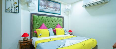 Un dormitorio ordenado con una tapizada verde acolchada, una cama con colcha amarilla y azul, dos lámparas de noche y un aire acondicionado instalado en la pared.