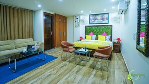 A hotel room with a bed, a sofa, a coffee table, and a dining table. - Lime Tree Hotel Near 32nd Milestone (Gurugram)