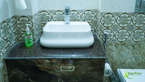 A bathroom with a white sink, a green bottle of soap, and a toilet. - Lime Tree Hotel Near 32nd Milestone (Gurugram)
