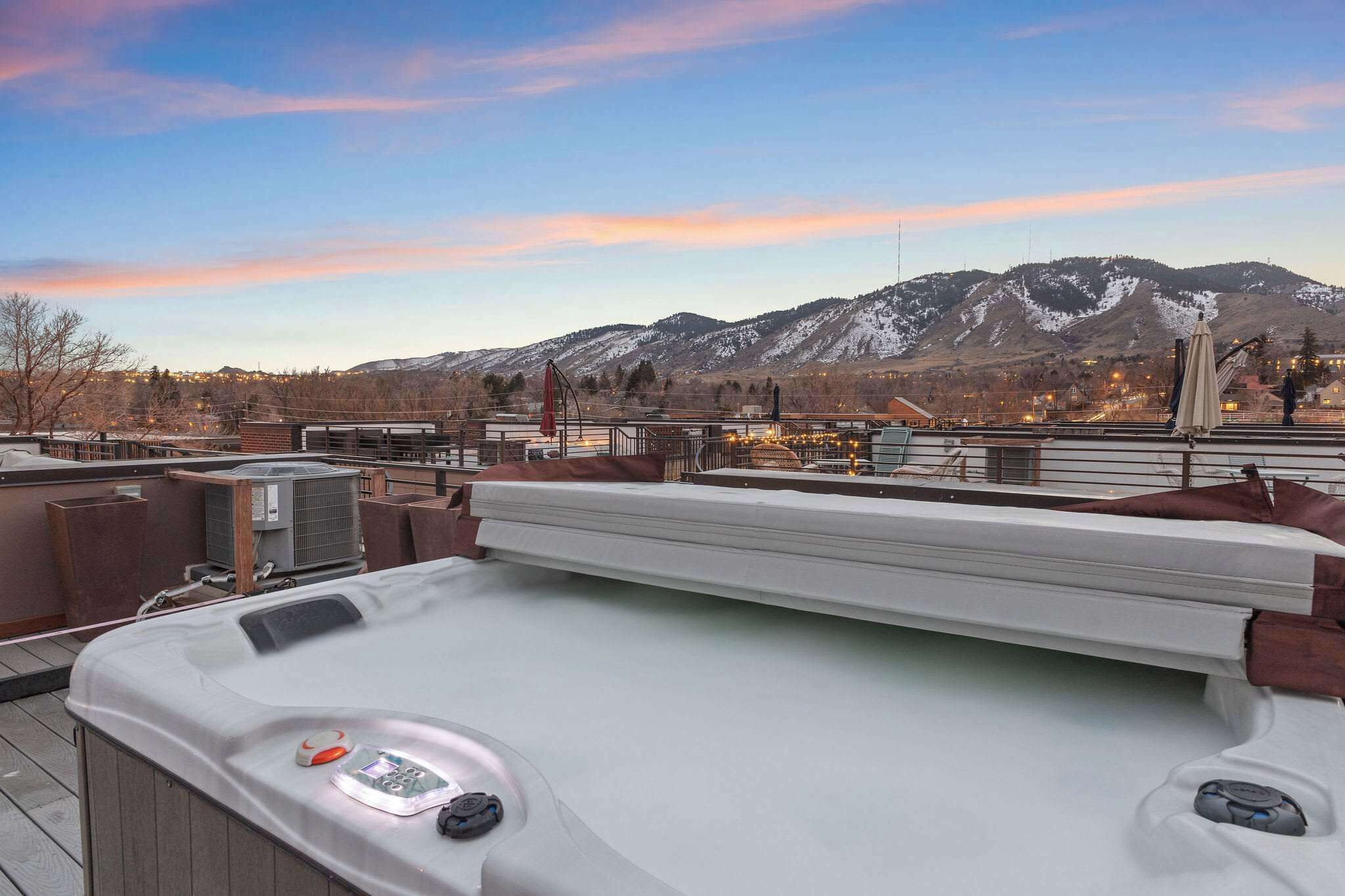 A rooftop terrace with a hot tub, outdoor seating, and a view of snow-capped mountains.
