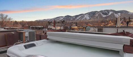 A rooftop terrace with a hot tub, outdoor seating, and a view of snow-capped mountains.