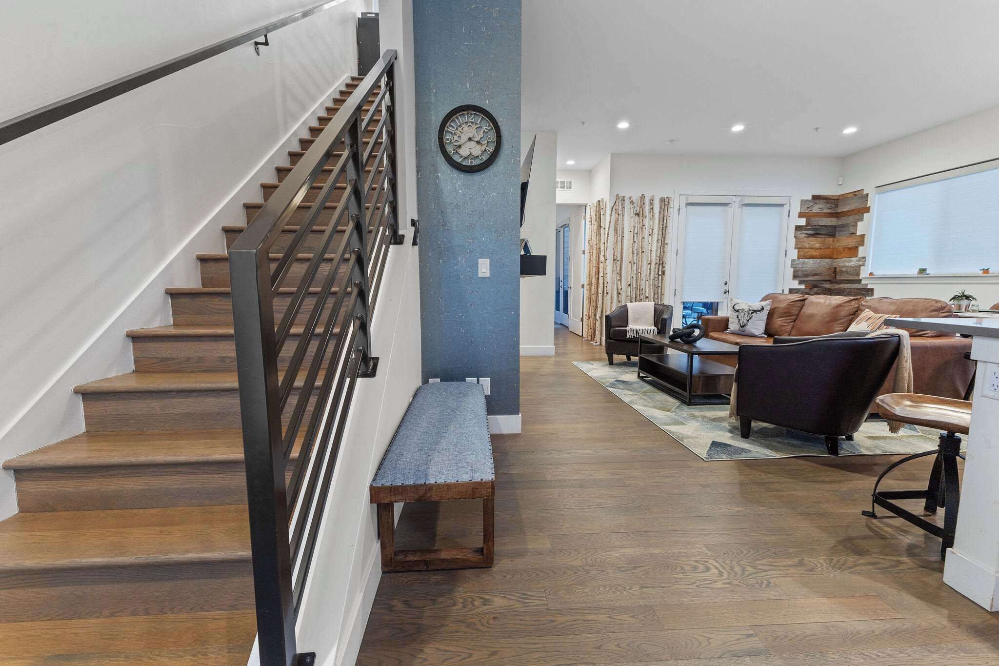 Un interior moderno con una escalera de madera, un banco, un sofá y una zona de comedor.