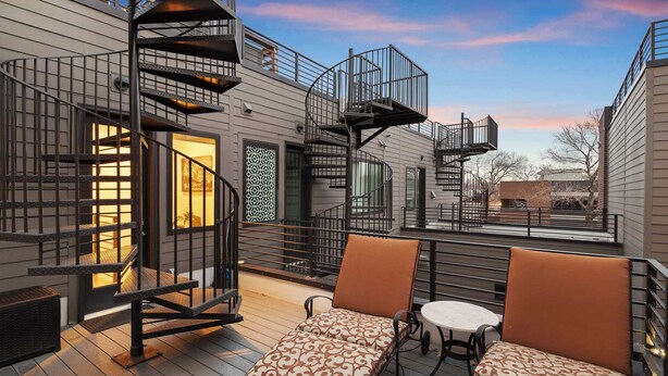 Eine Terrasse mit zwei gepolsterten Stühlen und einem kleinen Tisch, einer Wendeltreppe und einem Gebäude mit Fenster und Tür.